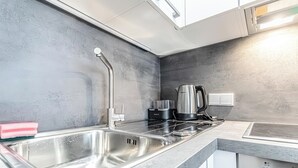 Eine moderne Küche mit Spüle aus Edelstahl, einem Wasserkocher und einem Einbauherd.