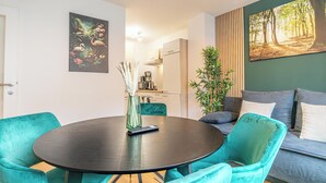Ein modernes Wohnzimmer mit türkisfarbenen Sesseln, einem dunklen runden Tisch und Kunstwerken an den Wänden.
