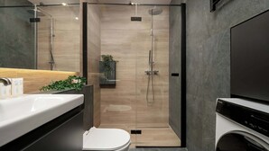 Une salle de bain moderne avec une douche à parois de verre, des toilettes, un lavabo avec un miroir et un lave-linge.