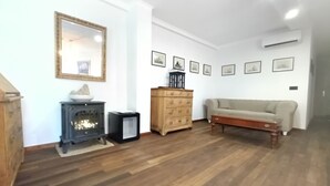 Een woonkamer met een houten vloer, een bank, een houten kast, een zwarte verwarming en een spiegel aan de muur.