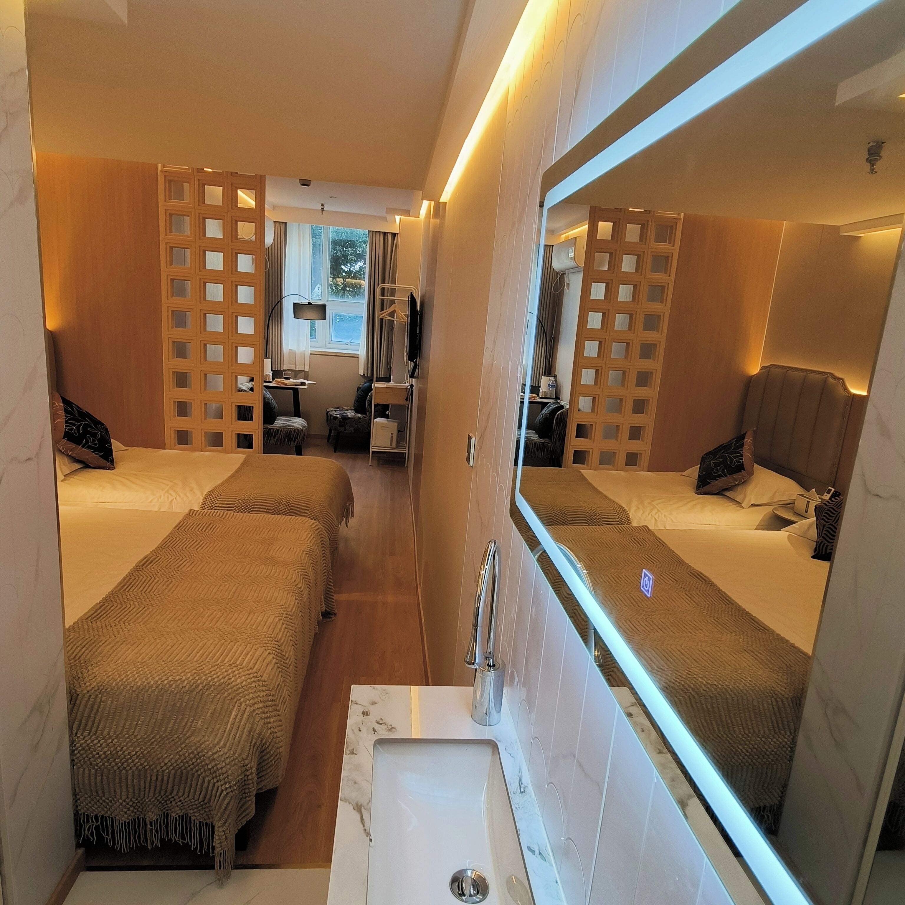 A compact hotel room with two beds, a small sitting area, and a large mirror.