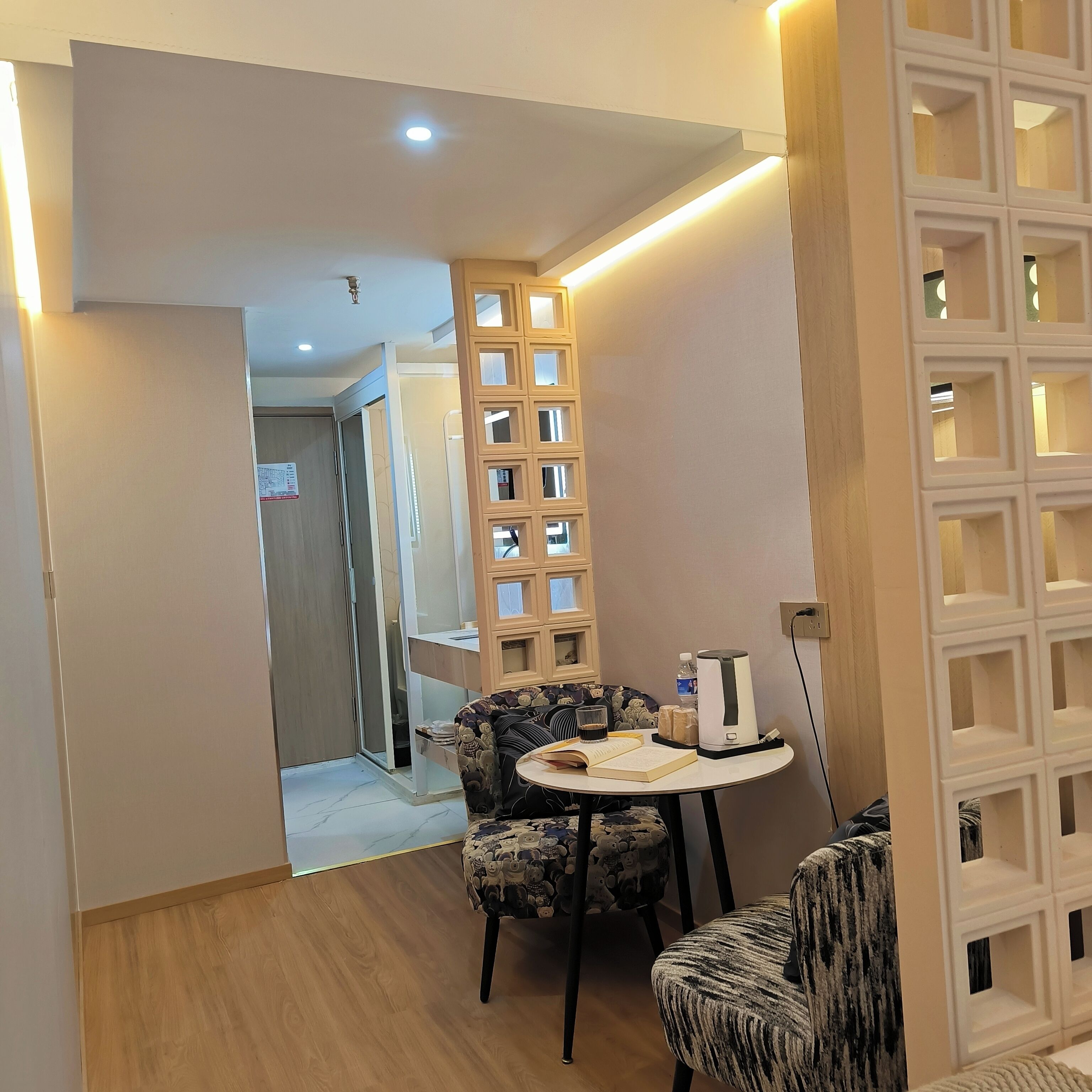 Quarto moderno com uma mesa redonda, duas cadeiras estampadas, um dispensador de água e uma tomada.