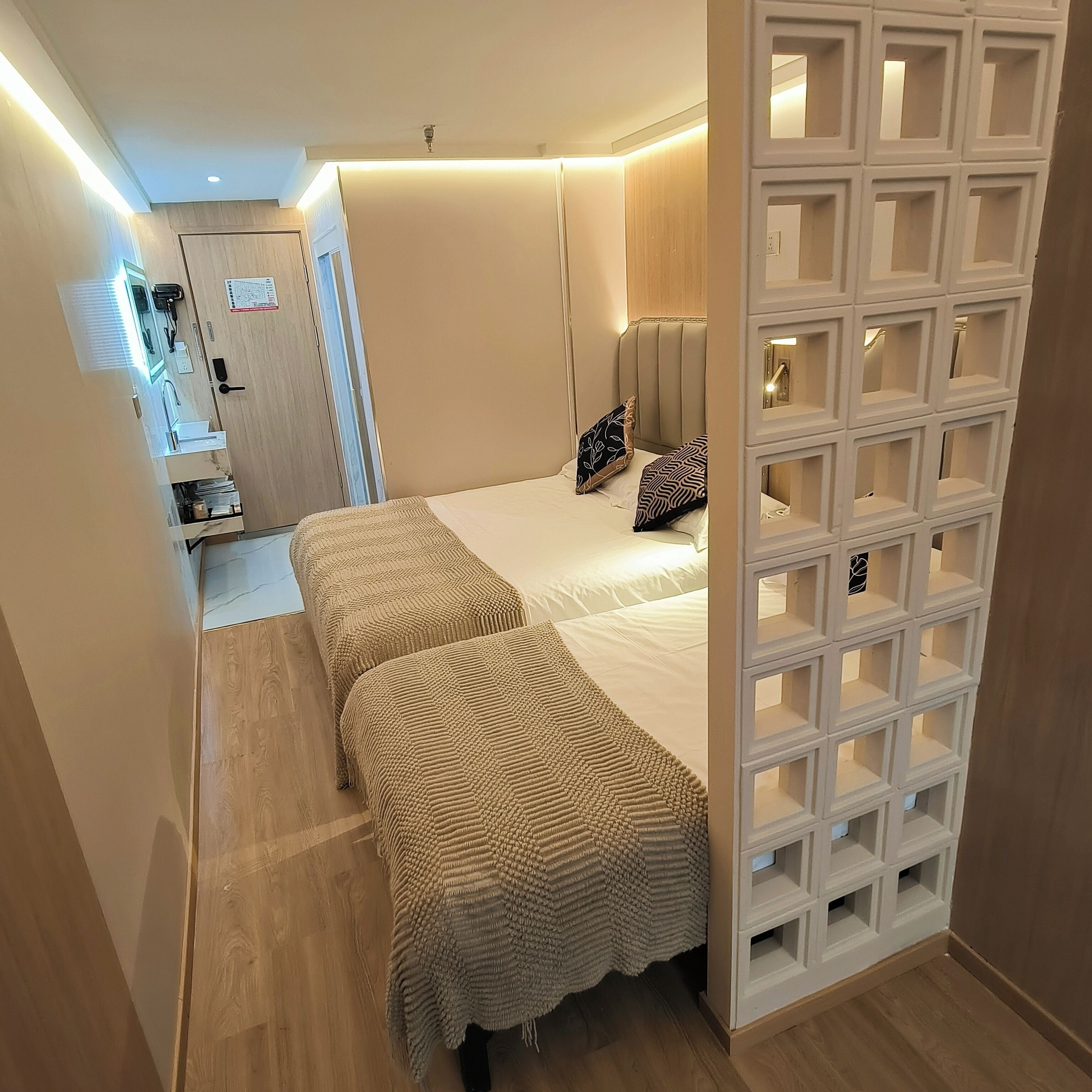 Un dormitorio con dos camas, un armario de madera, un escritorio con silla y un separador blanco con estantes.