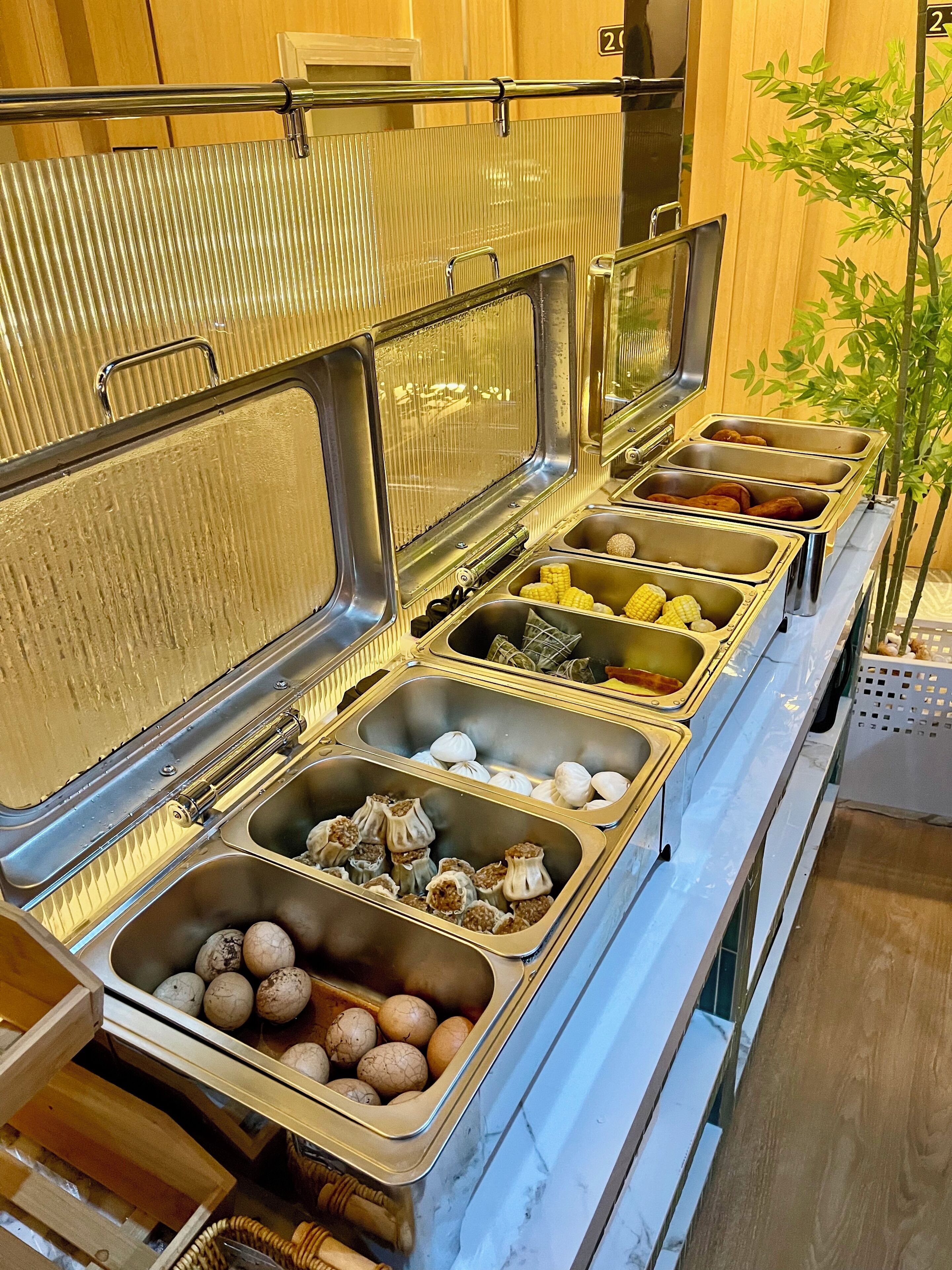 Montaje de bufé con varias estaciones de comida, que incluye opciones como maíz, dumplings y huevos.