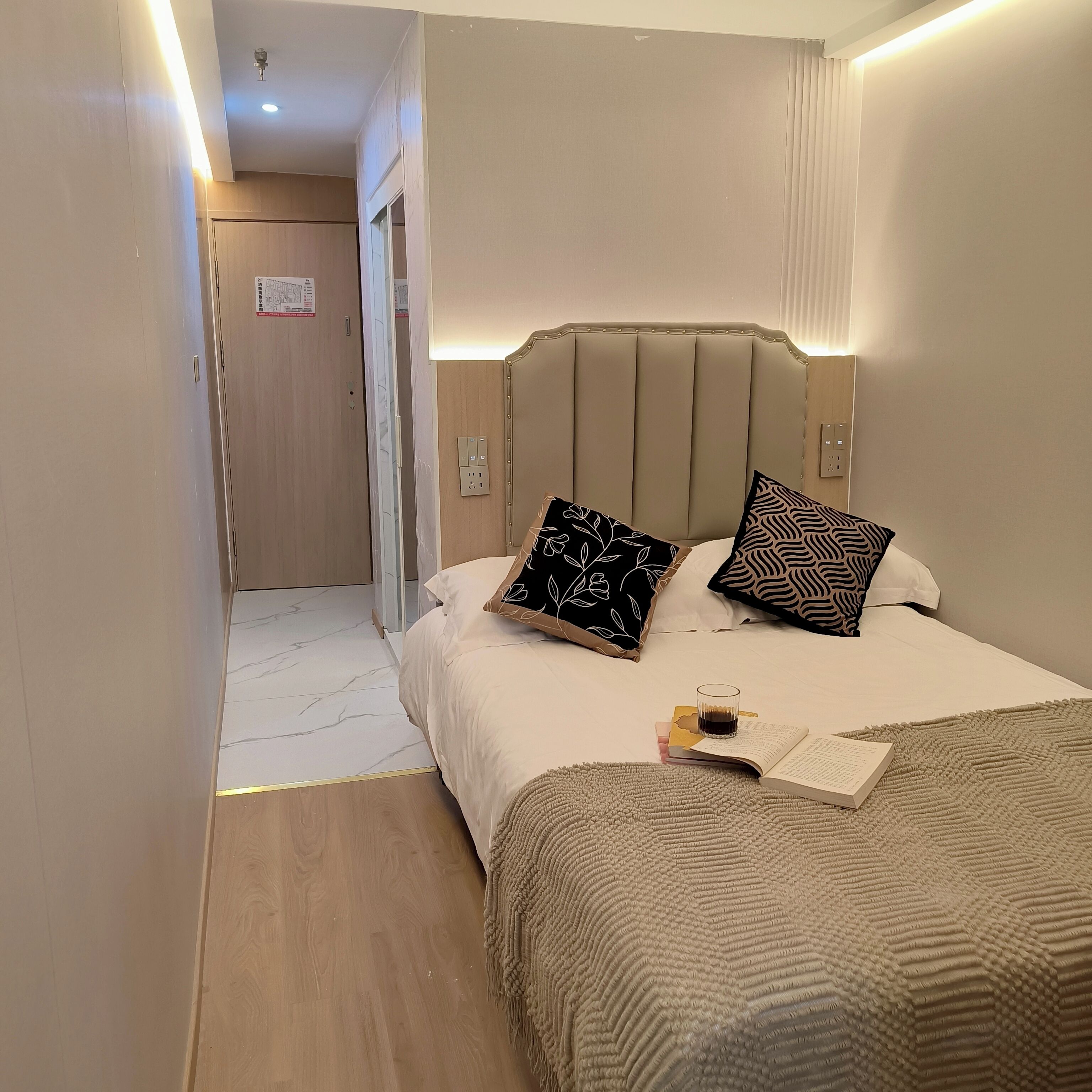 A hotel room with a bed, bedside table, and a mirror.