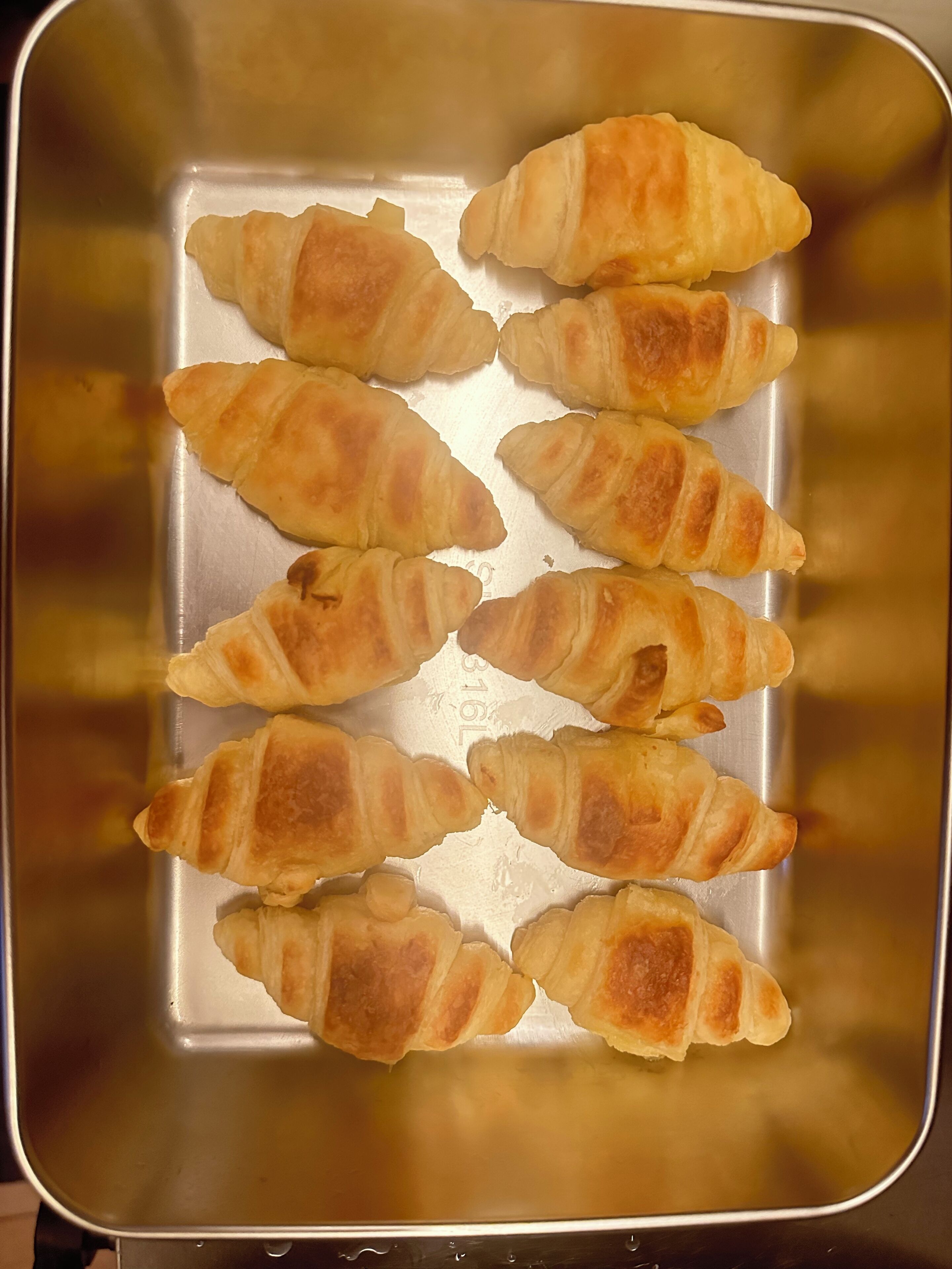Un plateau en acier inoxydable sur lequel sont disposés, de manière ordonnée, plusieurs croissants dorés et bruns.
