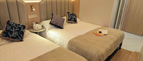 A hotel room with two beds, a bedside table with a lamp, and a small table with a phone and tissues.