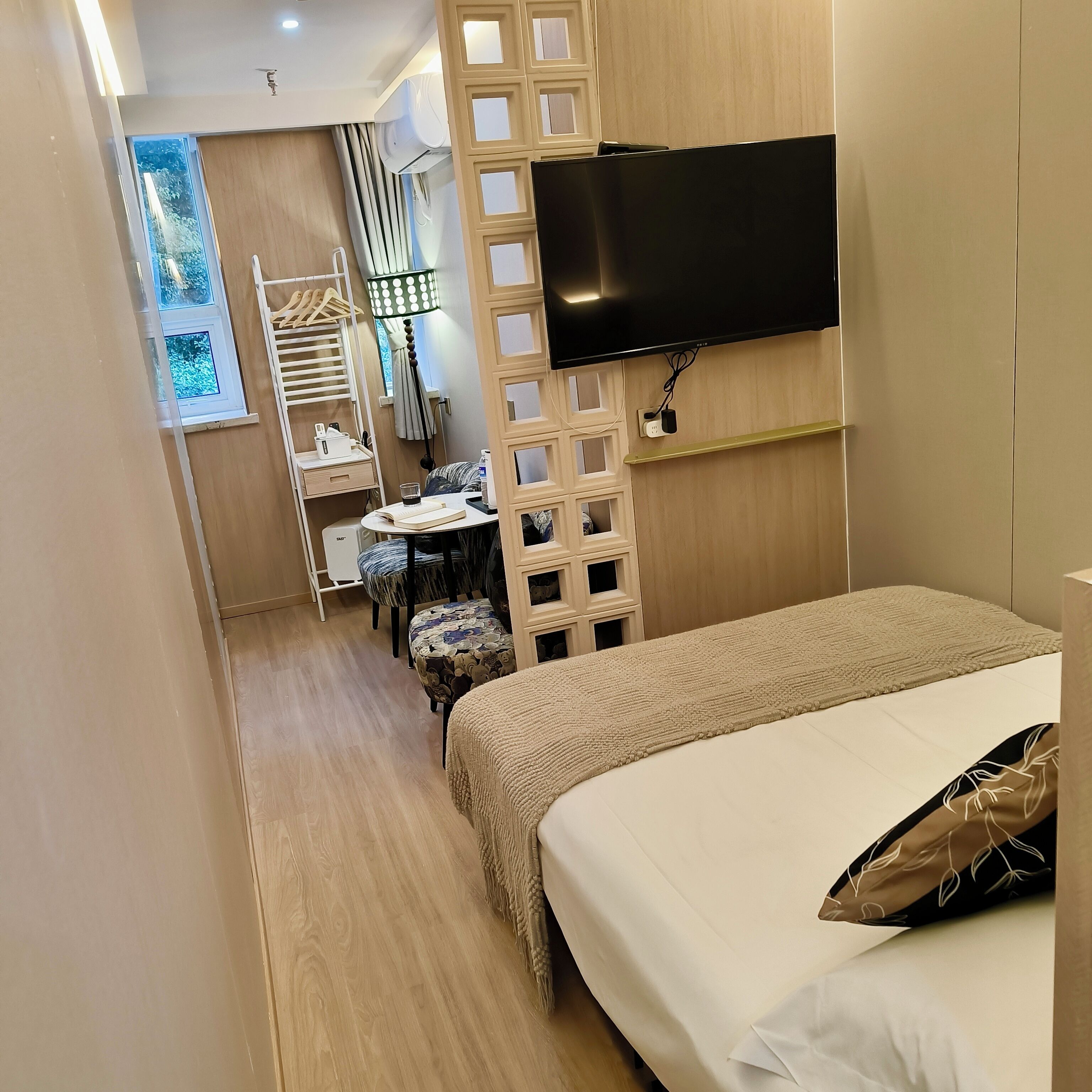 Una camera d'albergo con un letto, una TV fissata al muro, un tavolino con una sedia e una finestra con tende.