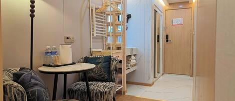 Une chambre d’hôtel moderne avec une table ronde, deux fauteuils à motifs, un lampadaire, une armoire intégrée et une porte en bois.