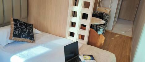 A hotel room with a bed, a laptop, and a book on the bed. There is a wooden floor, a white wall, and a door in the background.