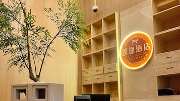 Un mostrador de recepción de hotel con un quiosco digital, un letrero de neón y una planta de bambú.