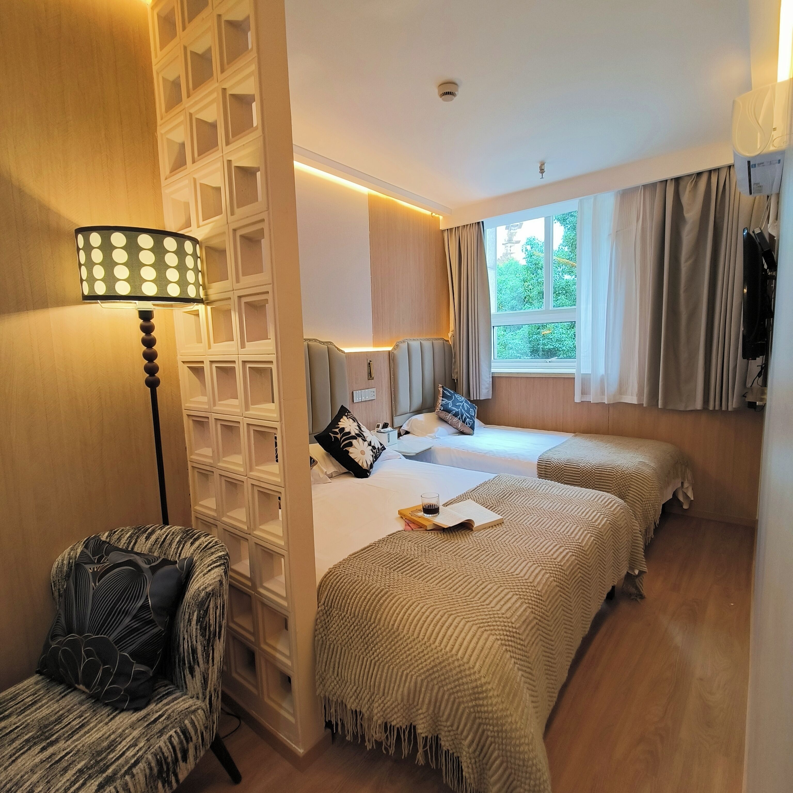 Habitación de hotel con dos camas, un escritorio, una silla, una lámpara y un ventanal con cortinas.