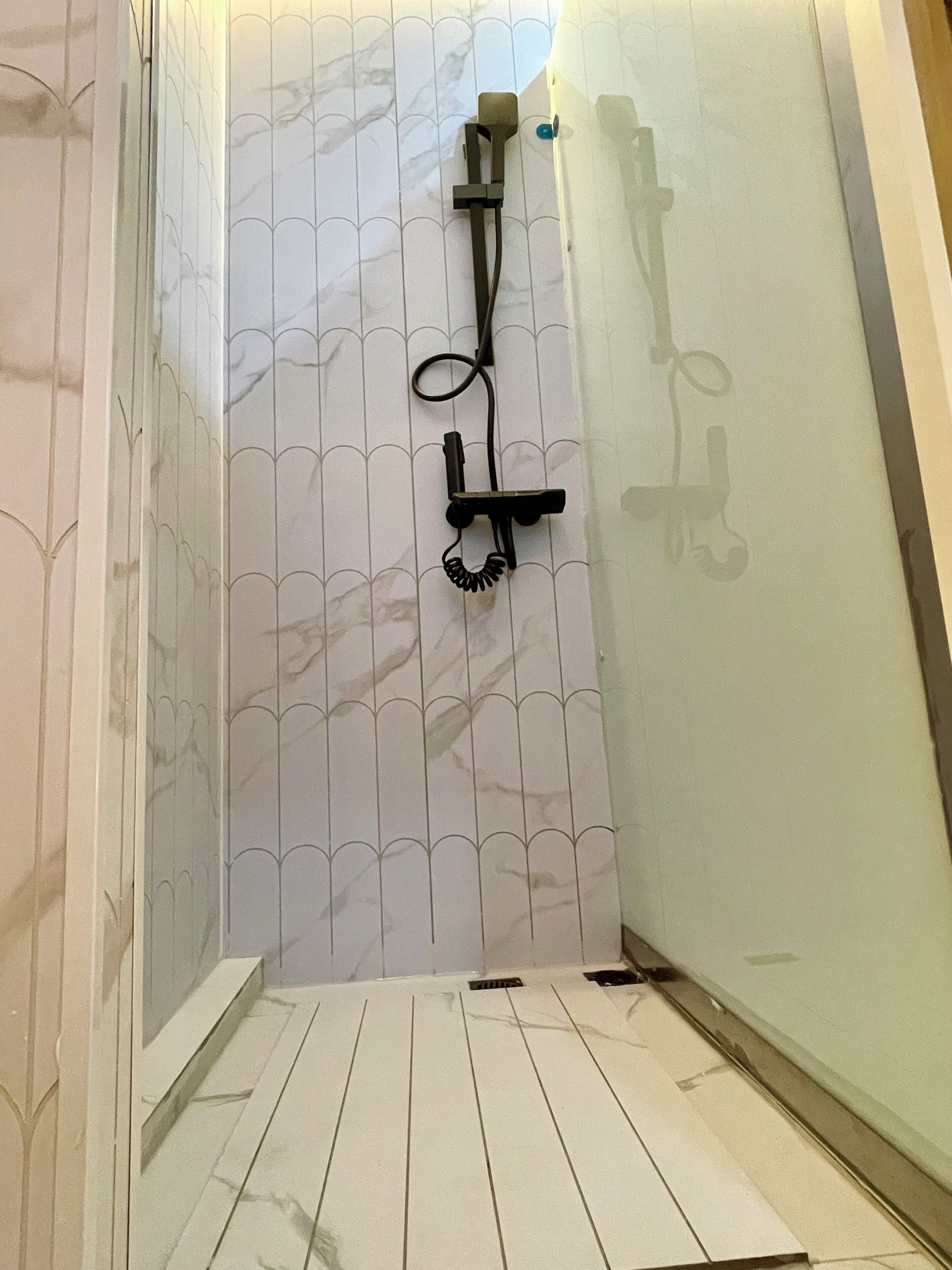 Un baño con pared de azulejos blancos, zona de ducha y suelo de madera.