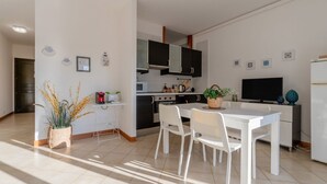 Een moderne keuken met witte kastjes, een eettafel met stoelen, een televisie en decoratieve objecten.