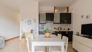 Een moderne keuken met witte kasten, een eettafel met stoelen, een televisie en een plant op de tafel.