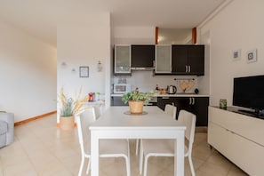 A modern kitchen with white cabinets, a dining table with chairs, a TV, and a plant on the table.