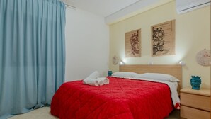 Een hotelkamer met een rood bed, een houten nachtkastje, een blauw gordijn en twee kunstwerken aan de muur.