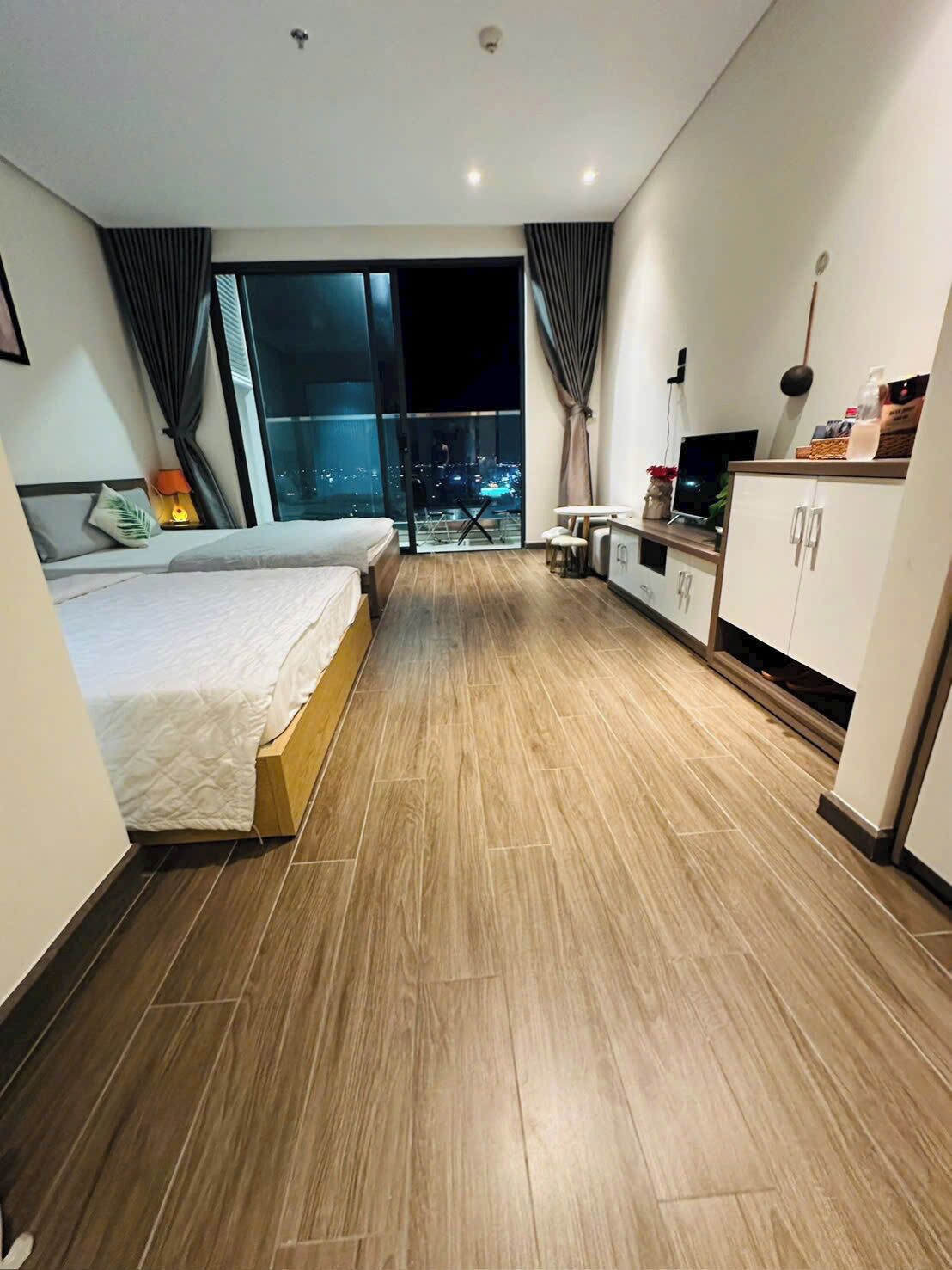 A modern hotel room with a large bed, a small kitchenette, and a balcony with a city view.
