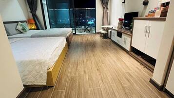 A modern hotel room with a large bed, a small kitchenette, and a balcony with a city view.