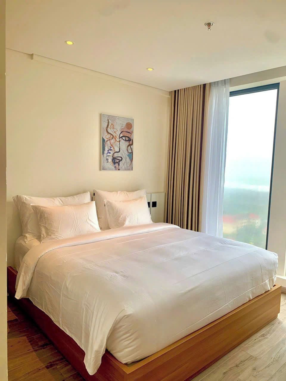 Un dormitorio moderno con una cama grande, un cuadro en la pared y vistas a través del ventanal.