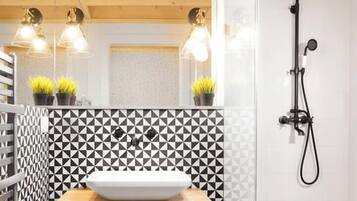 A modern bathroom with a geometric black and white tile backsplash, a wooden vanity with a sink, and a shower enclosure.