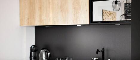 A modern kitchen with wooden cabinets, a black countertop, a coffee maker, a kettle, a microwave, and a sink.