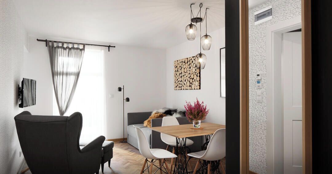 A dining area with a wooden table, white chairs, and a black sofa. There is a vase with flowers on the table, and a painting on the wall.