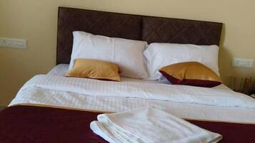 A neatly made bed with white bedding and two decorative pillows, a folded white towel, and a dark brown headboard.