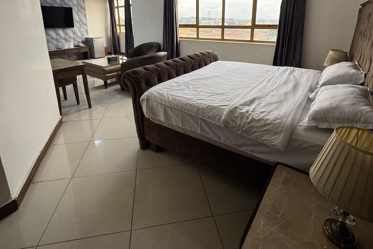 A hotel room with a large bed, a desk with a chair, a television mounted on the wall, and a window with curtains.