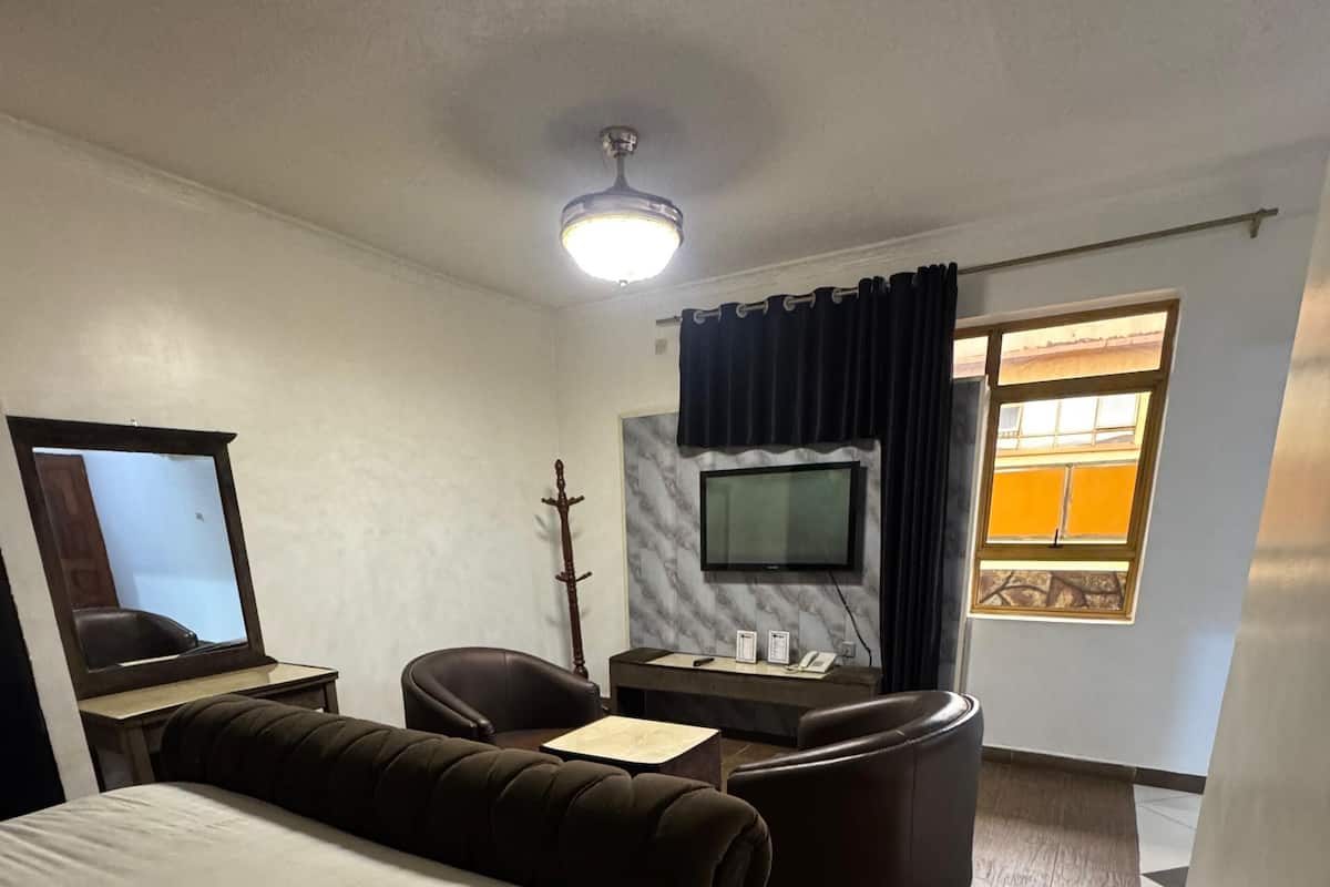 A hotel room with a bed, a desk with a chair, a television, and a window with curtains.