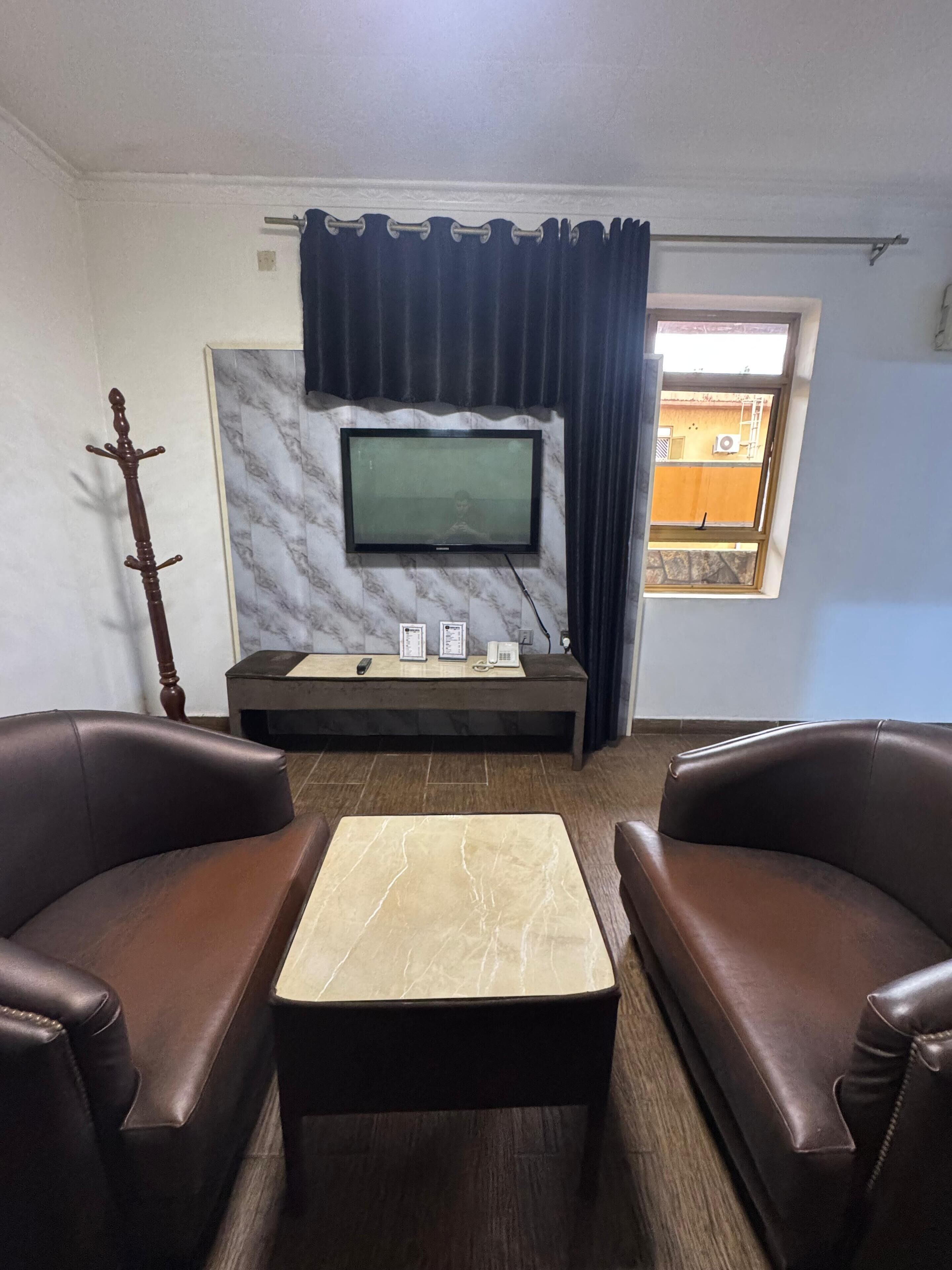 A living room with a television mounted on a marble wall, two leather sofas, a coffee table, and a window with curtains.