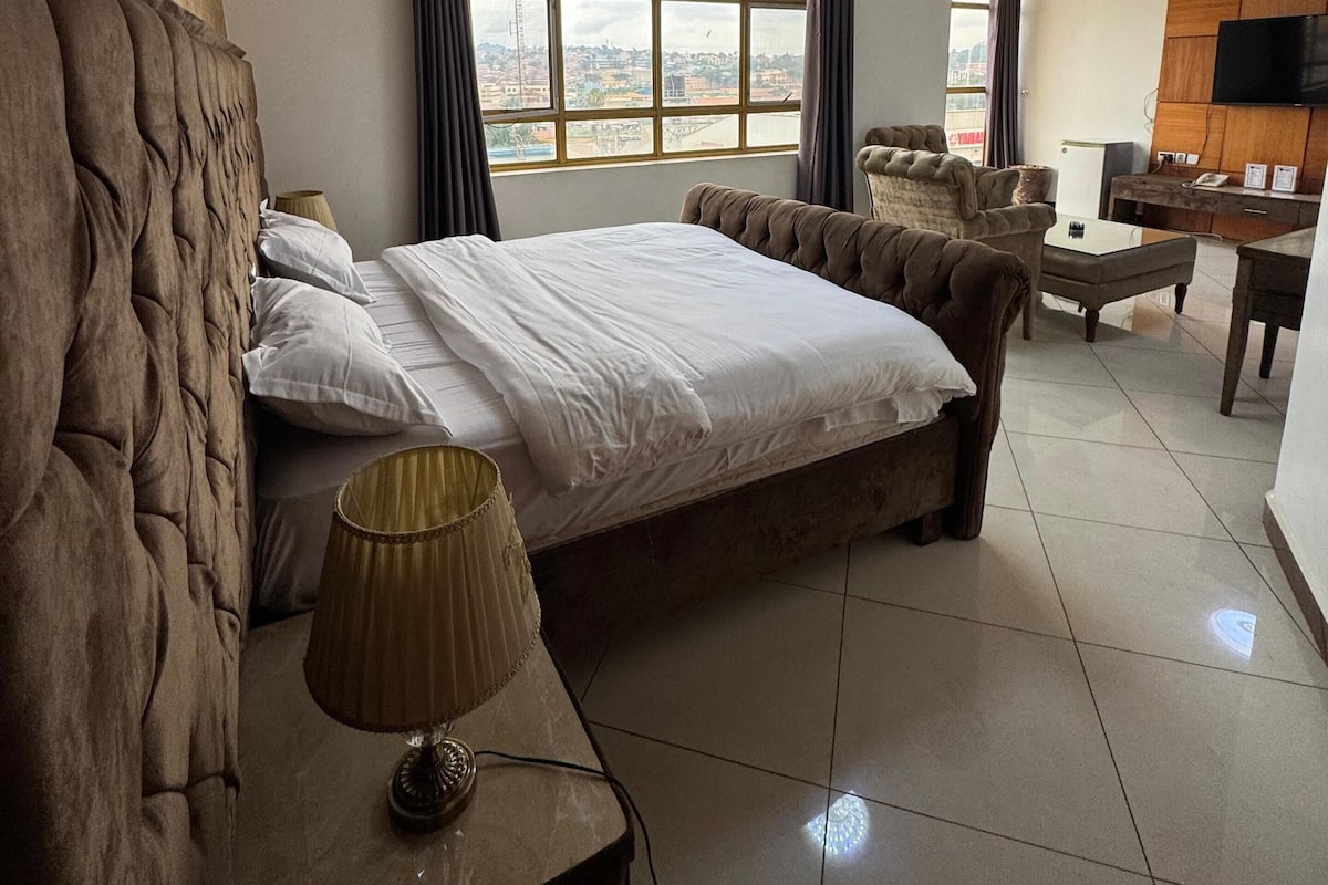 A hotel room with a large bed, a desk, a chair, a TV, and a window with curtains.