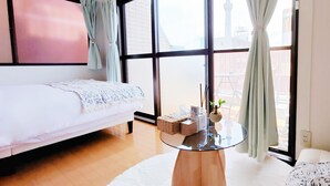 Una habitación de hotel moderna con una cama, una mesita redonda pequeña y un ventanal grande con cortinas.