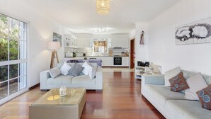 Un grand espace de vie comprenant un canapé, une table basse et donnant sur la cuisine et la salle à manger.