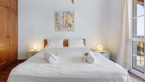 Un lit bien fait, avec deux serviettes enroulées, une tête de lit en bois, une œuvre d’art accrochée au mur et une lampe de chevet.
