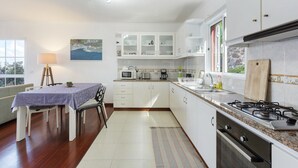 Une cuisine moderne avec des meubles blancs, un coin repas comprenant une table et des chaises, et une vue sur l’extérieur.