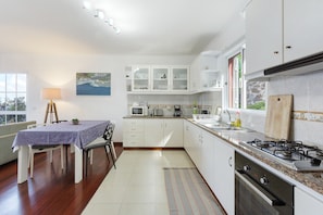 Una cocina moderna con armarios blancos, un comedor con mesa y sillas, y vistas al exterior.