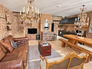 Amplia sala de estar con sofá de cuero, mesa de centro de madera, mesa de comedor con bancos, candelabro y pared de ladrillo.