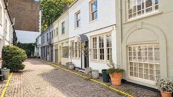 A cobblestone street lined with white buildings, some with arched windows and doors, and potted plants along the sidewalk.