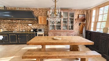 A rustic kitchen with a wooden table and bench, a chandelier, and brick walls.