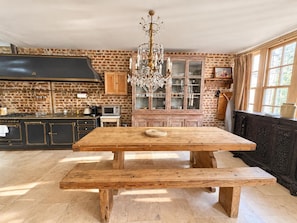 A rustic kitchen with a wooden table and bench, a chandelier, and brick walls. - Knightsbridge 2BR Mews House (London)