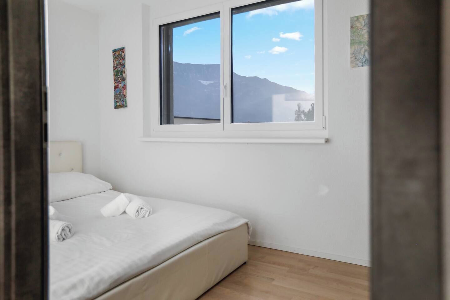 Une chambre avec un lit, une fenêtre donnant sur la montagne et un petit tableau accroché au mur.