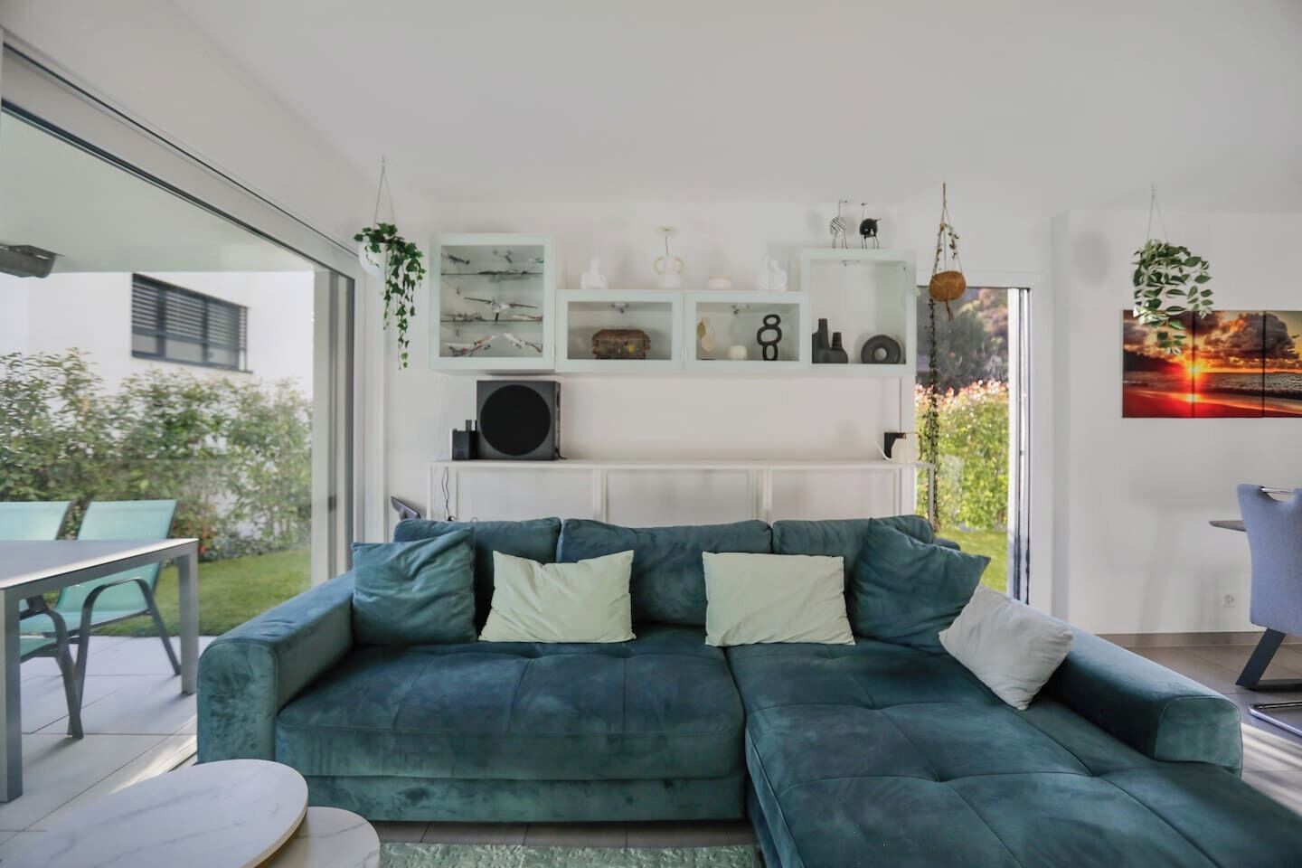 A modern living room with a teal sectional sofa, a dining area with a table and chairs, and a view of the outdoors.