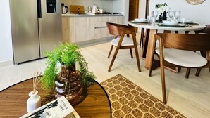 Una cocina moderna con refrigerador empotrado, un comedor con una mesa redonda y sillas, y una sala de estar con sofá y mesa de centro.