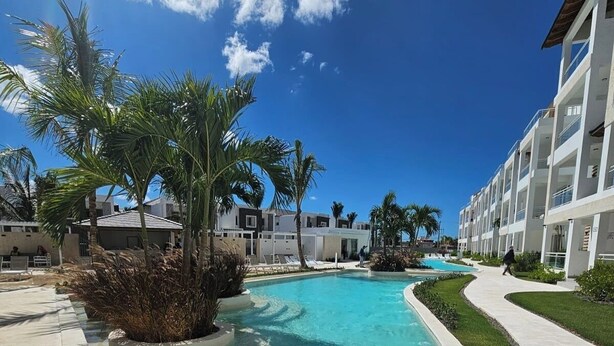 Piscina de resort con agua cristalina, rodeada de palmeras y un edificio moderno con balcones.