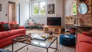 En stue med en rød sofa, et glasbord, et fjernsyn og en bogreol.