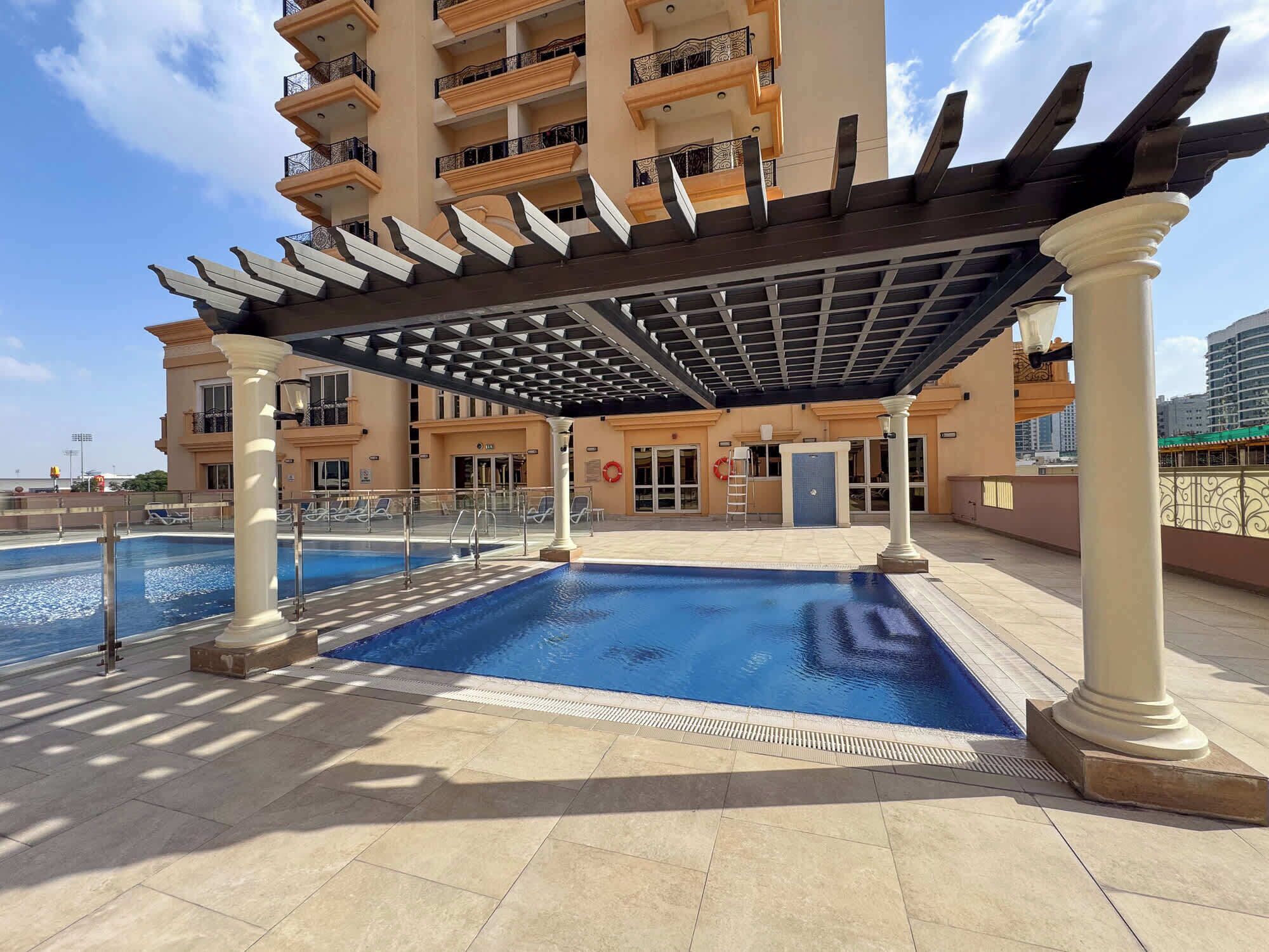 Una piscina en la azotea con pérgola, columnas y vista de un rascacielos al fondo.