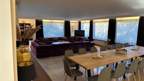 A modern living room with a large purple sofa, a wooden dining table with chairs, and a television. - House Anna Alpirsbach (Alpirsbach)