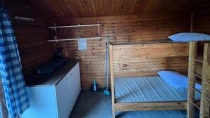 Una pequeña cabaña de madera con literas, una kitchenette y una estantería con un cartel.