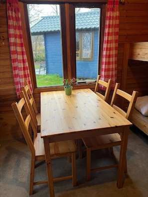 Una mesa de madera con sillas, una planta en maceta y una ventana con cortinas.